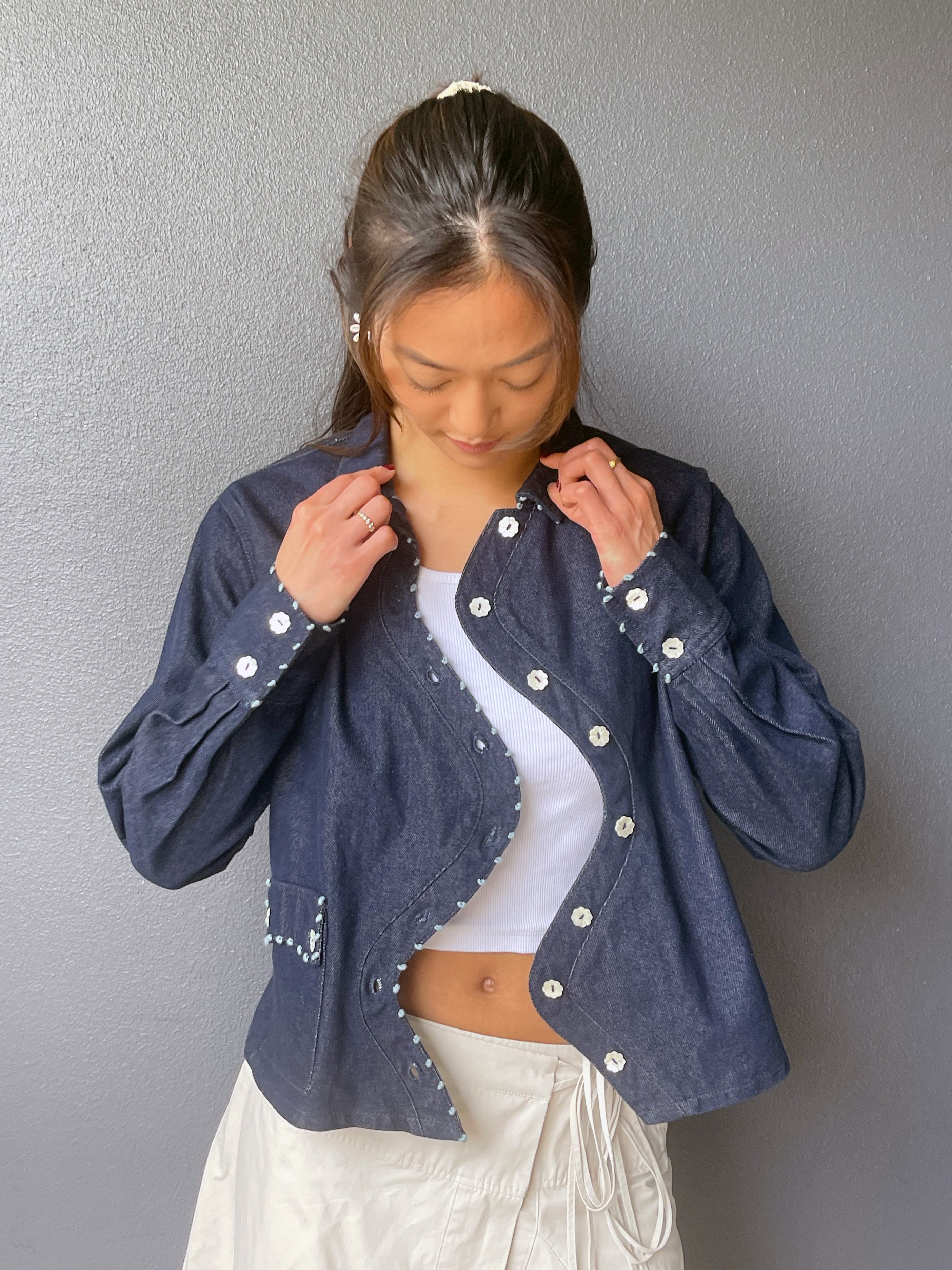 Model wearing the Say the Label Wave Denim Jacket open over a white top, styled with white trousers