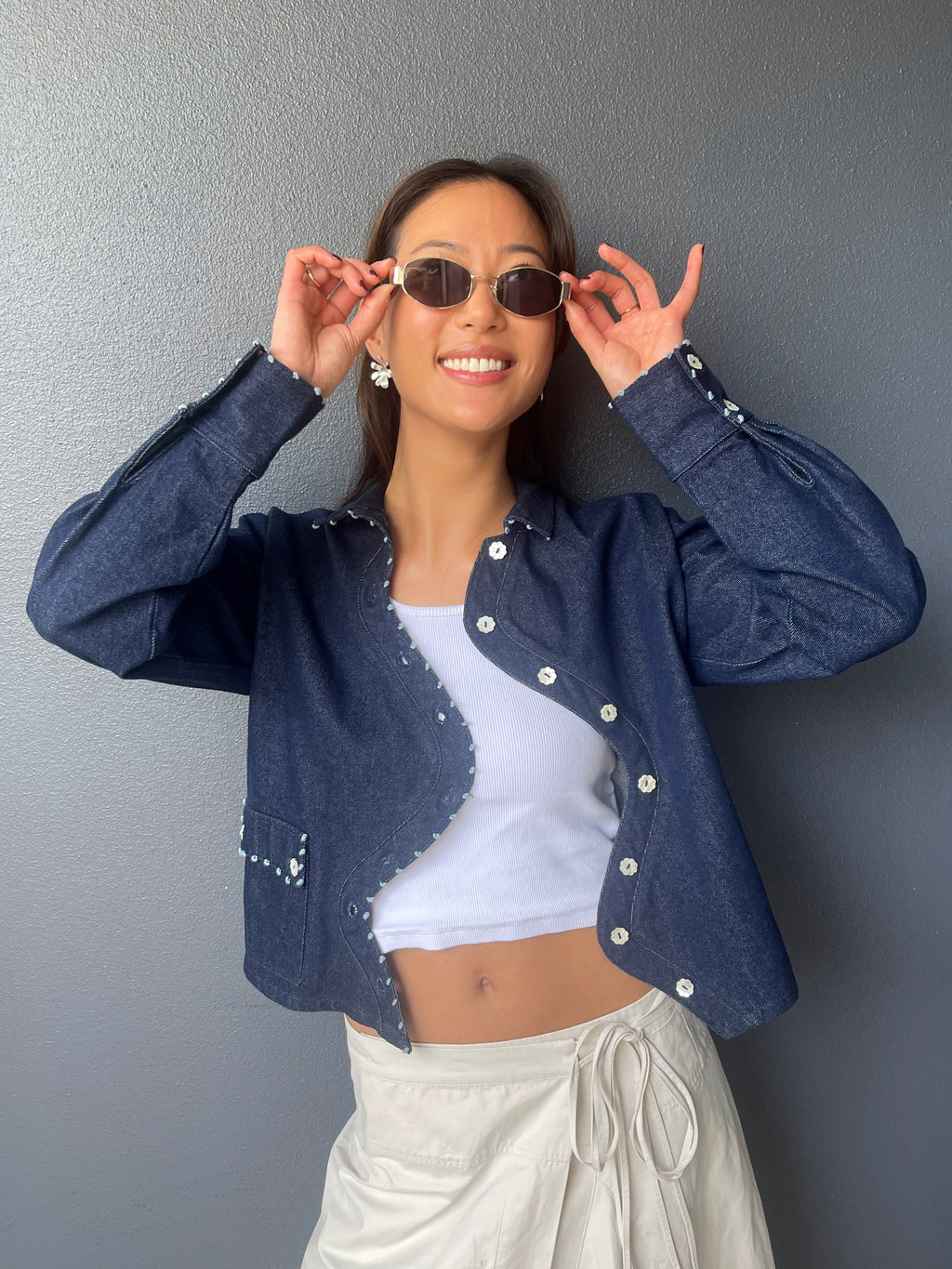 Model in sunglasses wearing the Say the Label Wave Denim Jacket over a white top with cream trousers